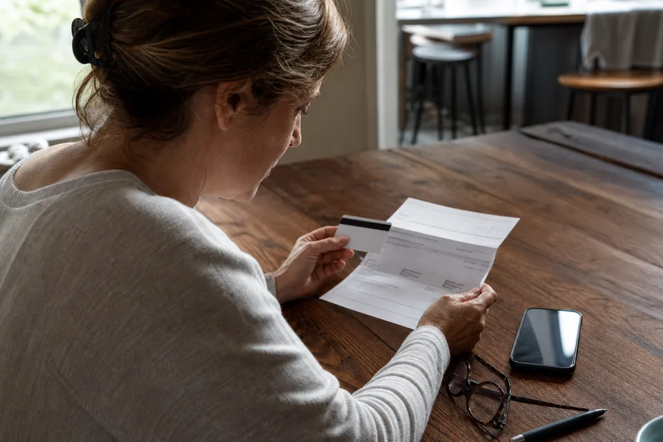A woman at a kitchen table with an insurance card, a phone and a printed statement