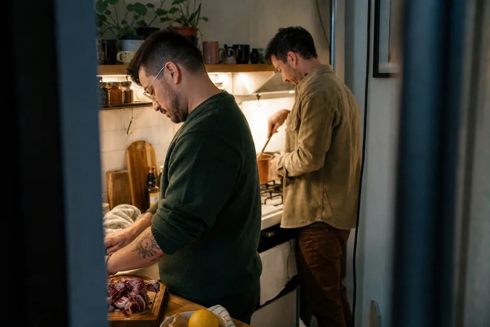 Two adult men cooking together in a small apartment kitchen in the evening