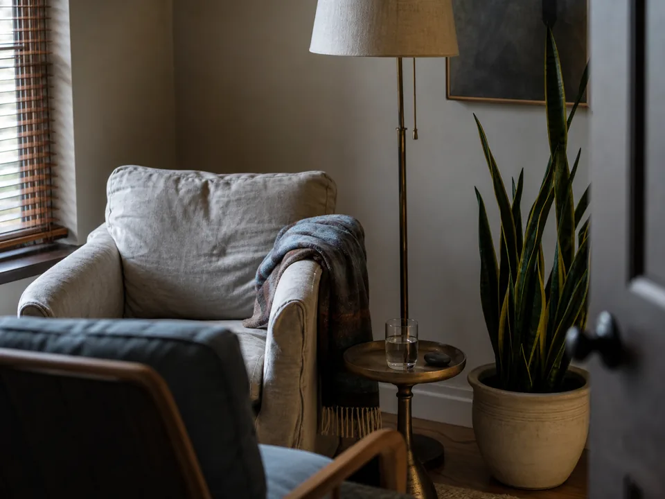 Detail of a therapy room armchair with a folded blanket, a lamp and a small table with a glass of water, soft window light